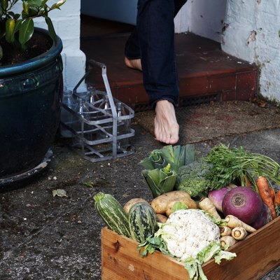 Low section of person walking towards crate of vegetables outside house