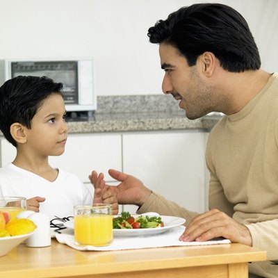 Man and boy sitting at table in kitchen, with salad and orange juice on table and man talking to boy, close-up