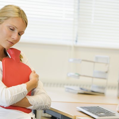 Businesswoman hugging heating pad at desk