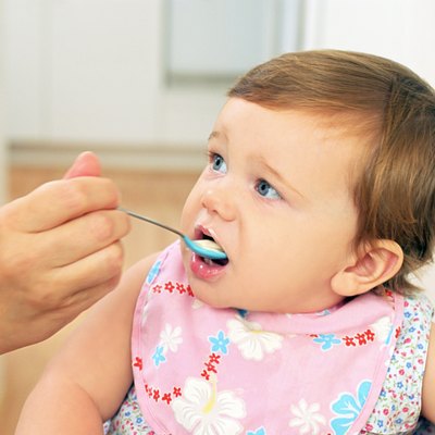A baby girl looks to her mother as she is fed with a spoon.