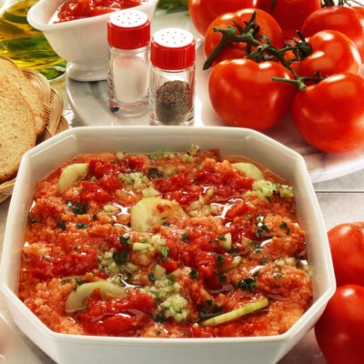 close-up of a tomato based dish served beside whole tomatoes and bread
