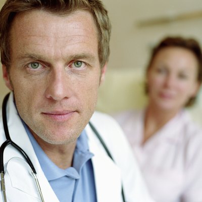 Mature male doctor by female patient lying in hospital bed, portrait