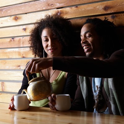 Man and woman drinking tea at table in cafe, smiling