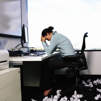 Woman sitting at desk by crumpled papers on floor