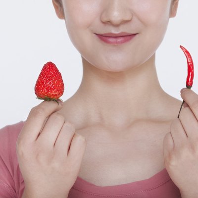 Young woman smiling and holding opposites, a strawberry and a chili pepper, in each hand