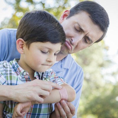 Loving Father Puts Bandage on Elbow of Young Son