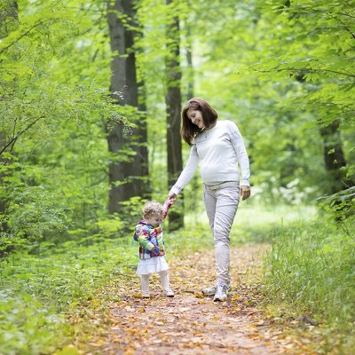 Beautiful pregnant woman and her baby daughter walking in park