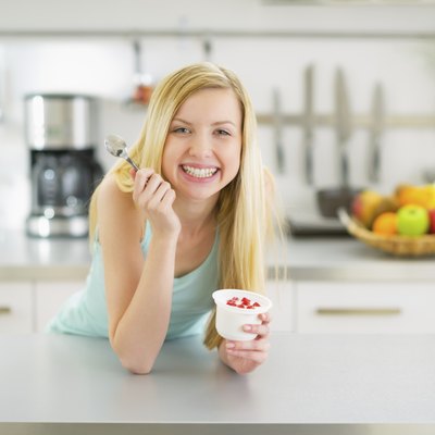 happy young woman eating yogurt in kitchen
