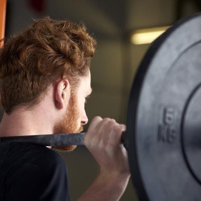 Rear View Of Young Man In Gym Lifting Weights On Barbell