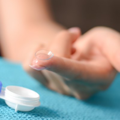 Soft contact lens on woman's fingertip with open case