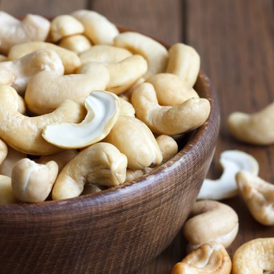 Wooden bowl of cashew nuts from above. On dark wood.