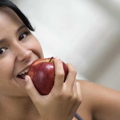 Smiling teenage girl eating apple, close-up, tilt