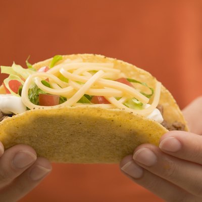 Hands holding a taco filled with mince and cheese