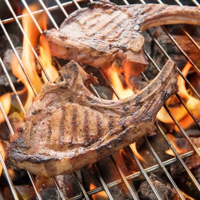 Grilled pork steaks over flames on the grill.