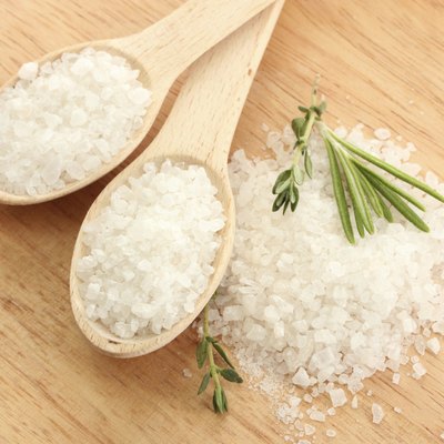 salt in spoons with fresh rosemary and thyme on table