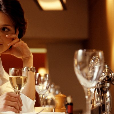 Woman sitting at table in restaurant, holding glass of wine, close-up