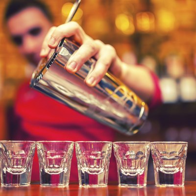barman pouring cocktail drinks into shot glasses