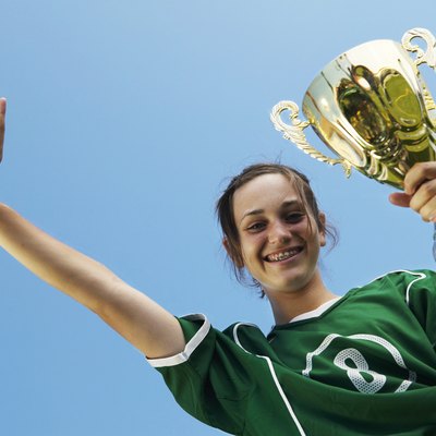 Female (11-13) footballer with trophy, other hand raised, smiling