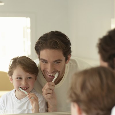 Father and son (5-7) brushing teeth, looking at reflections in mirror