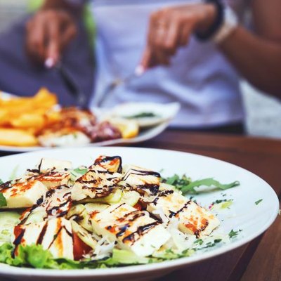 Dinner at restaurant. Close-up salad with grilled cheese. People eating on the background