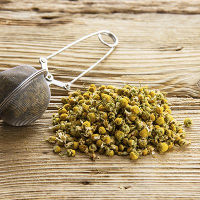 Dry camomile with tea strainer on old wooden table