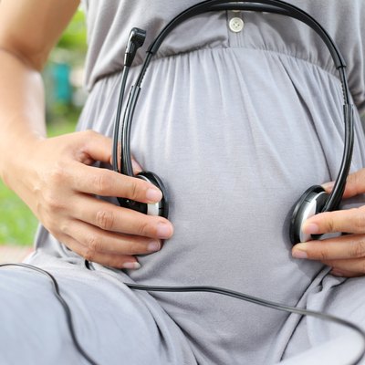 Pregnant women put earphone in hand on her belly.