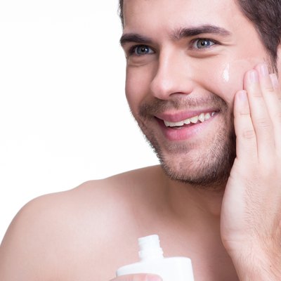 Young happy man applying cream.