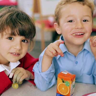 Schoolgirl and boy (4-6) at table, smiling, close-up, portrait