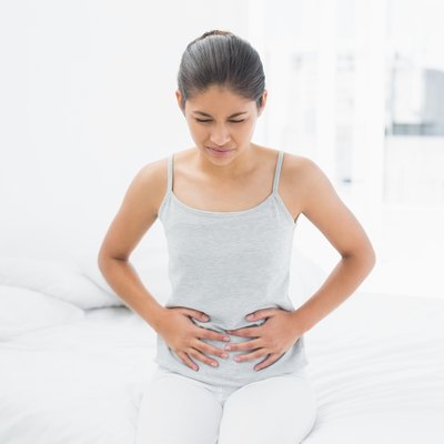 Casual woman with stomach pain sitting in bed