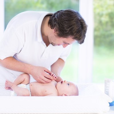 Young father talking to newborn baby relaxing on changing table