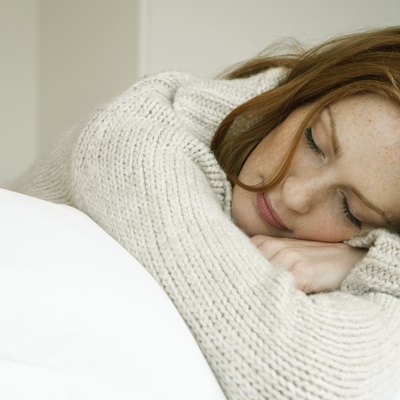 Young woman lying on bed, resting head on arms, eyes closed, close-up