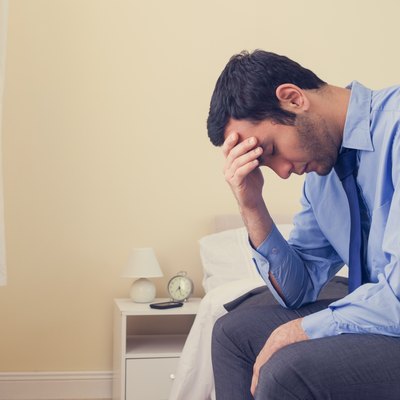 Depressed man sitting head in hands on his bed