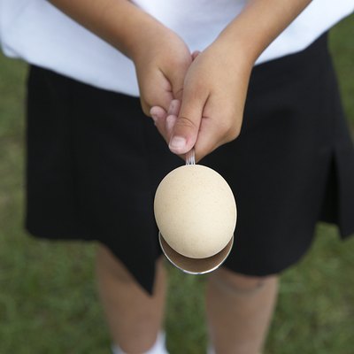 Girl (5-7) standing in field holding egg on spoon, mid section