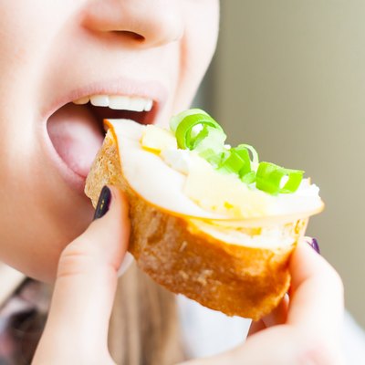woman eating sandwich with cheese and green vegetables onion