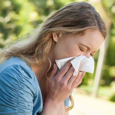 Woman blowing nose with tissue paper at park