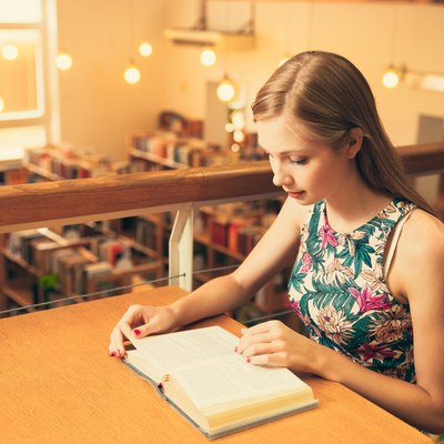 Beautiful young woman student in library reading a book
