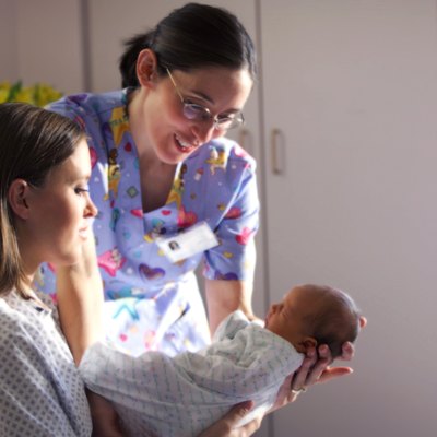 a caucasian mother shows off her newborn baby to a nurse while recovering in a hospital bed