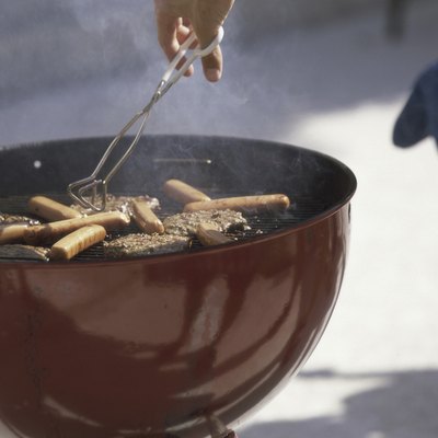 Person using tongs on hamburgers and hot dogs cooking on a barbecue grill