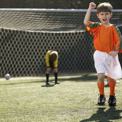 Boy in soccer uniform celebrating, defeated goalkeeper in background (portrait)