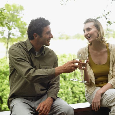 Couple sitting on balcony toasting each other with drinks, smiling