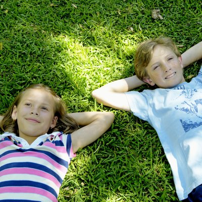 Girl and boy (9-11) lying on grass, hands behind heads, smiling