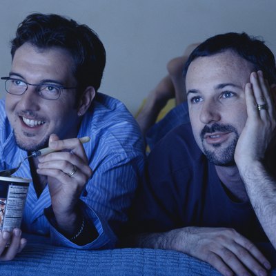 Gay couple lying on bed watching television, one eating ice cream