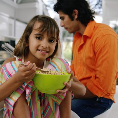 Dad with newspaper at table, girl (8-10) with bowl of cereal, portrait