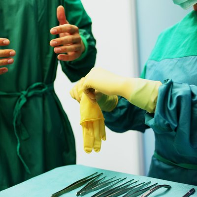 Operating theatre staff wearing scrubs,one helping other put on gloves