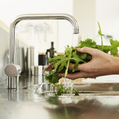 Young woman washing lettuce at kitchen sink, close-up of hands