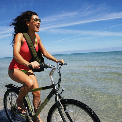 Young woman riding bicycle on beach, smiling, side view