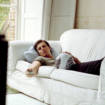 Man lying on sofa using television remote control