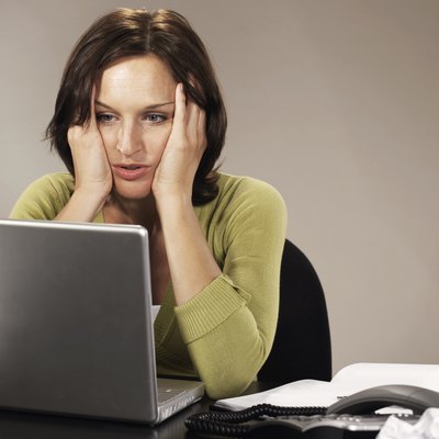 Woman sitting at laptop, elbows on desk, holding head in hands