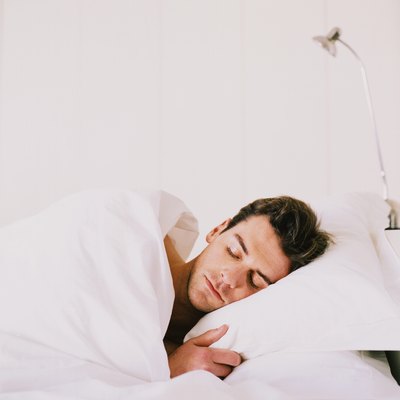 Young man sleeping with duvet covering him in bed