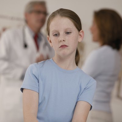 Sick girl sitting in doctor's office while mother and doctor talk in background